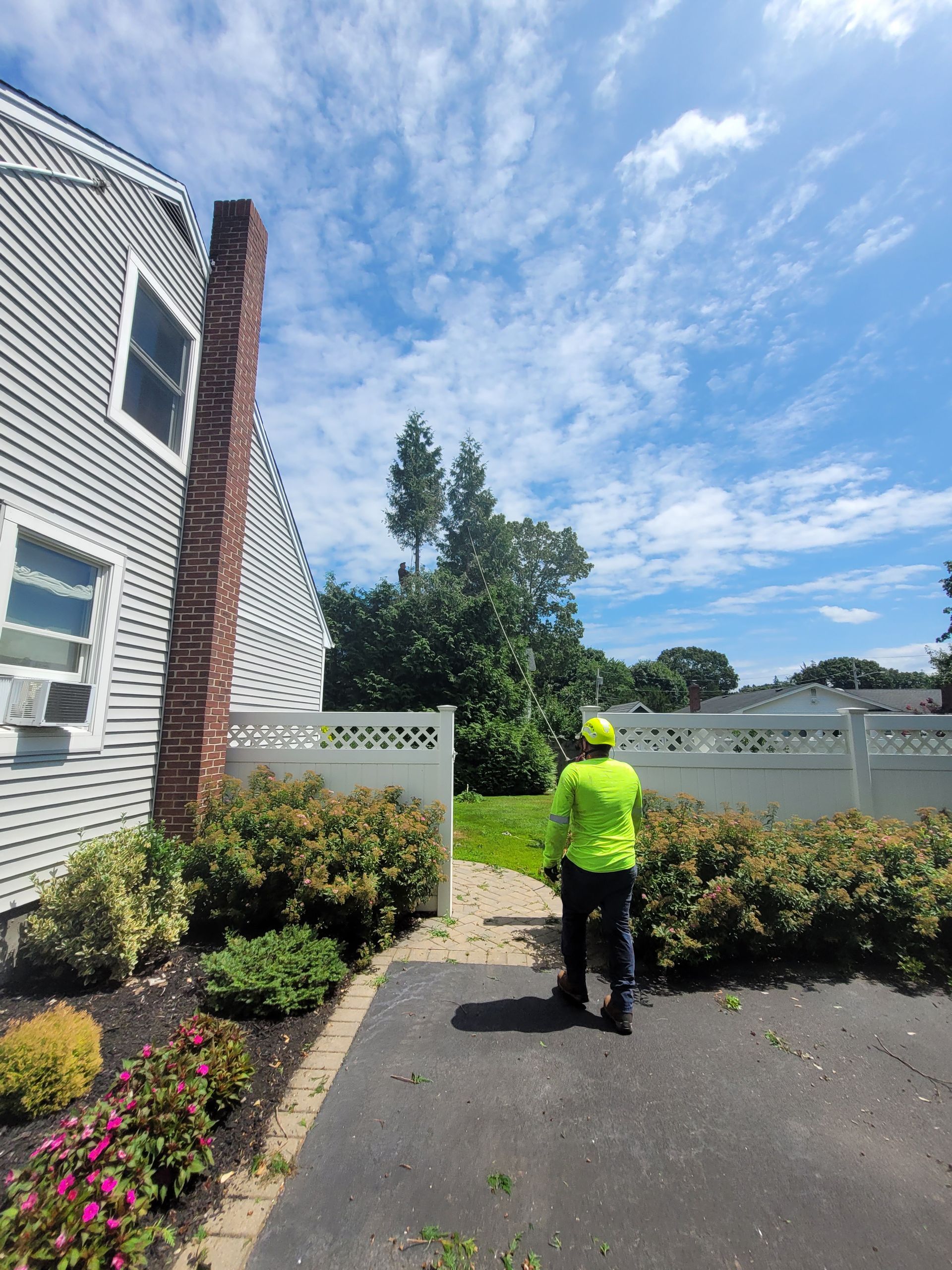 Person in neon green shirt walking on a paved path beside a house and shrubs under a blue sky