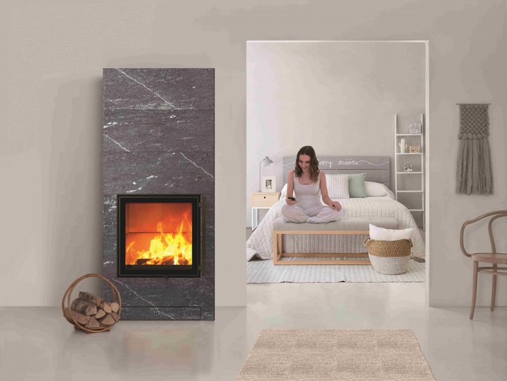 Camera da letto moderna con camino, grande specchio e una donna seduta su un letto con lenzuola bianche.