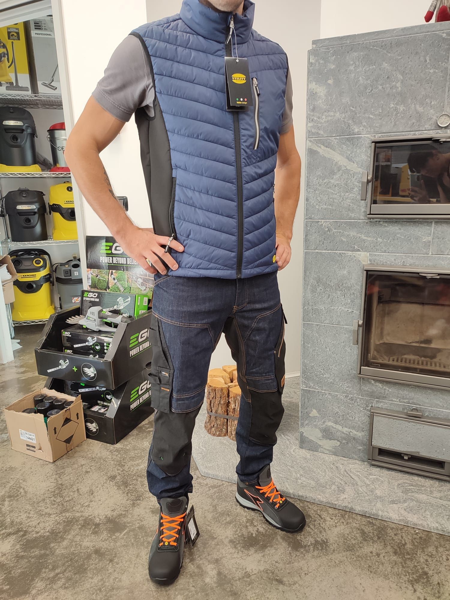 Persona con gilet imbottito blu e scarpe da trekking in piedi in una corsia di un negozio.