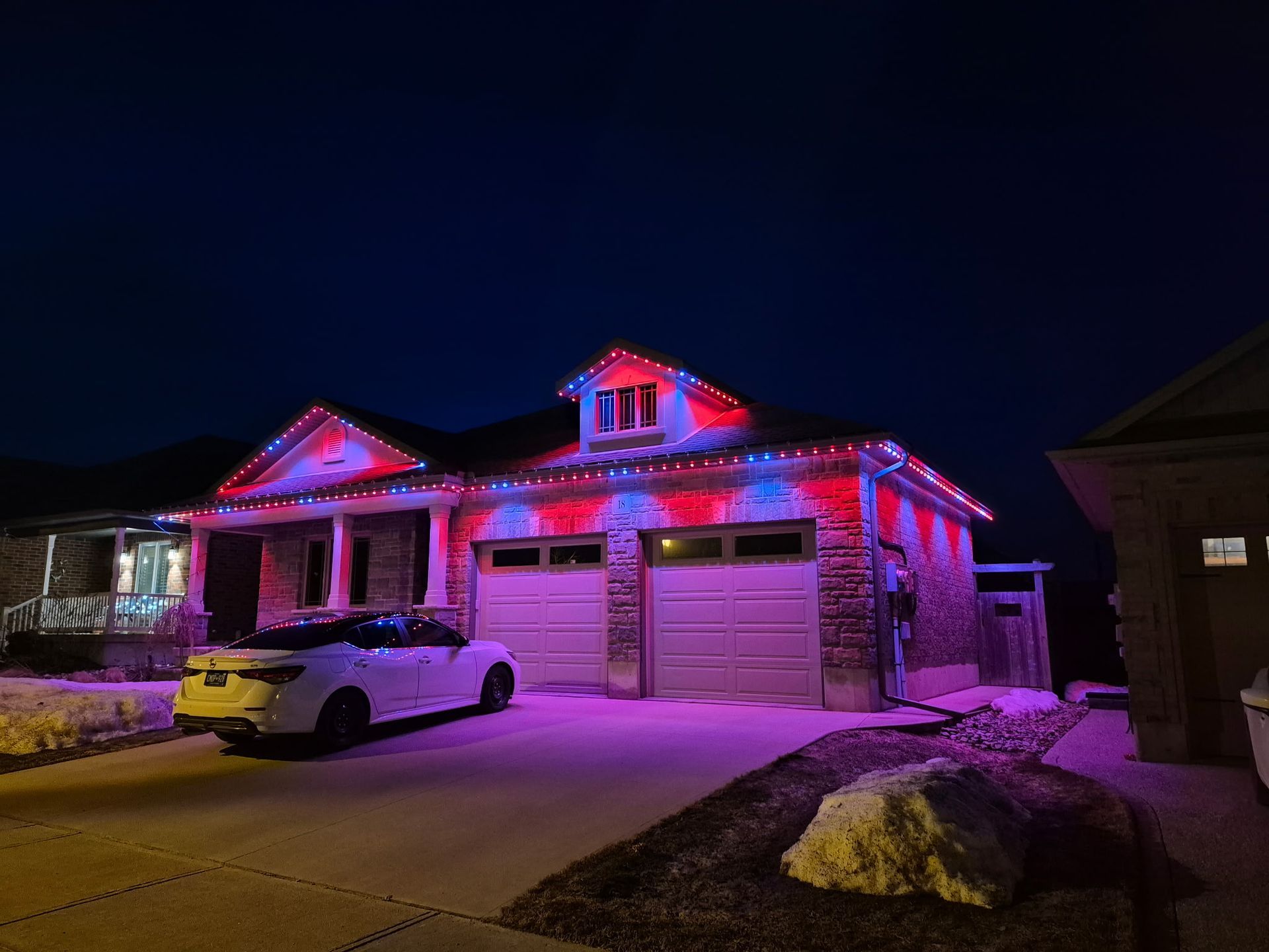 House lit with red and blue holiday lights at night, with a car parked in the driveway.