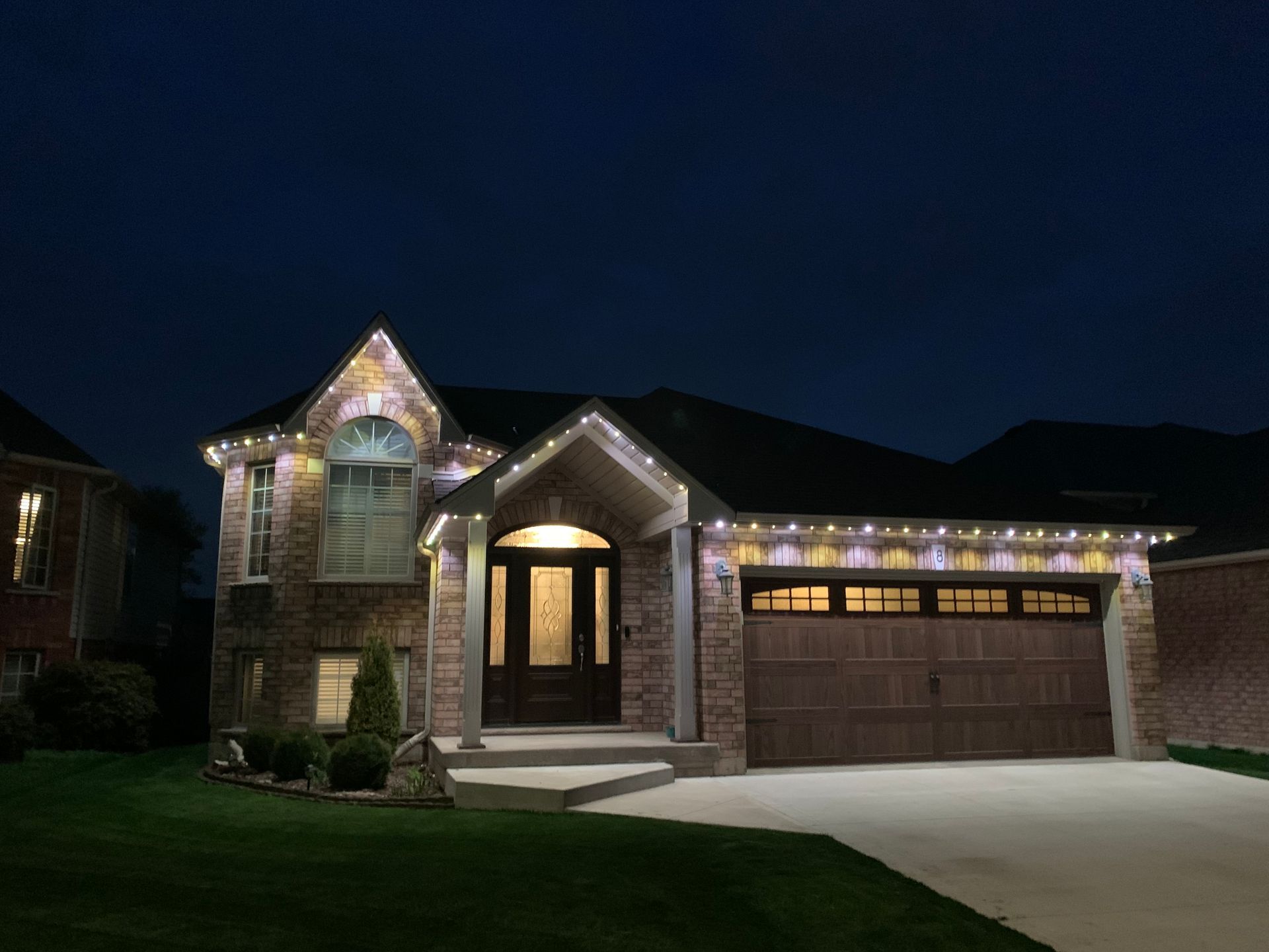Suburban brick house at dusk with warm porch lights and a three-car garage