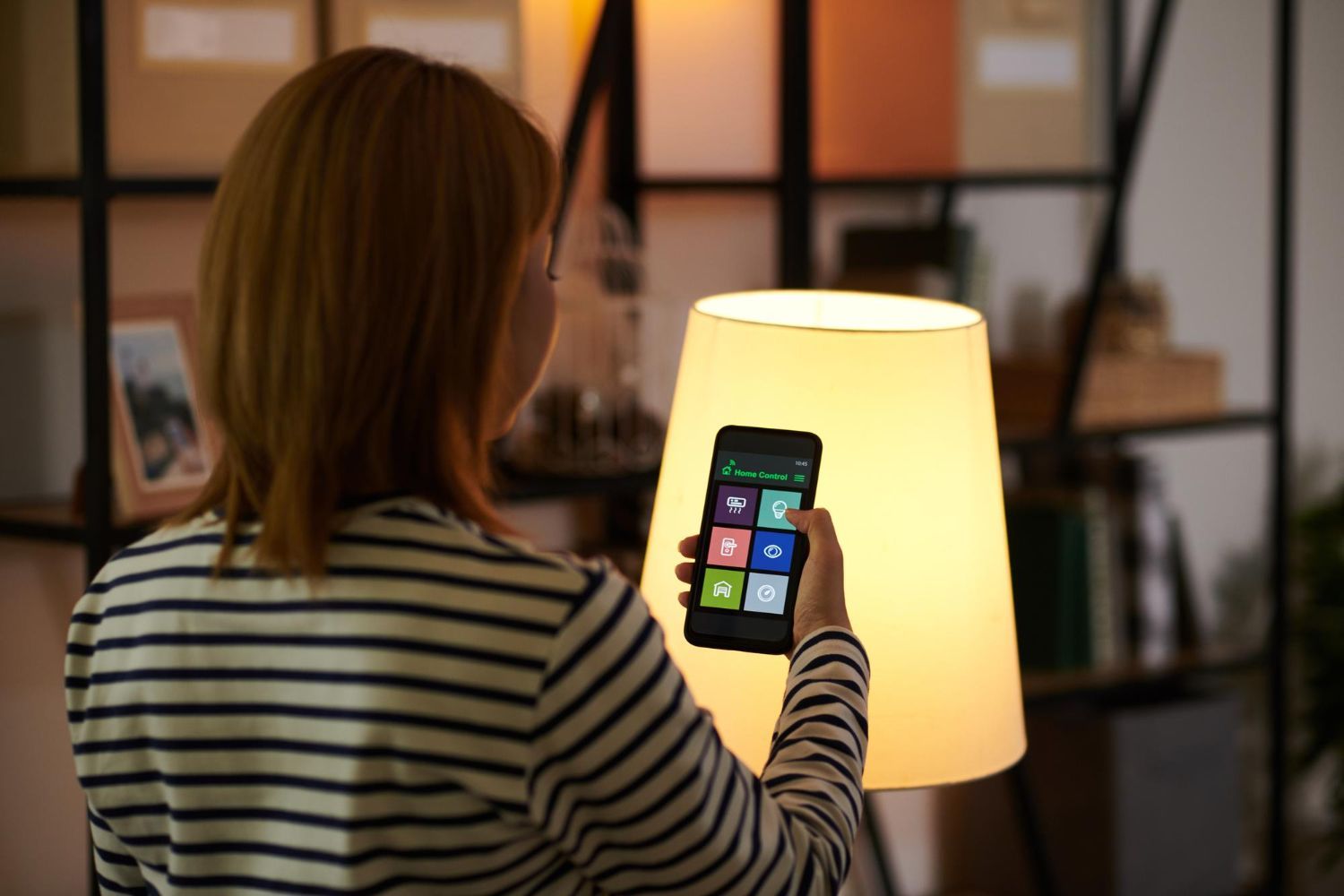 Person using a smartphone to control a glowing lamp in a dim room