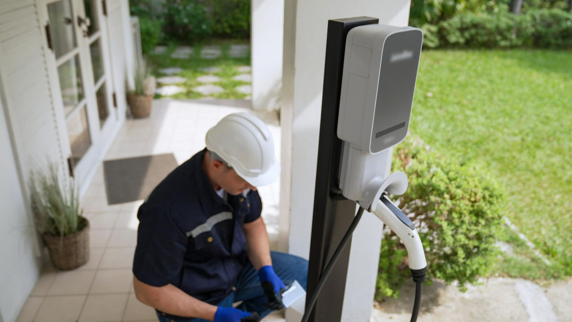 A man is sitting on the ground working on an electric vehicle charging station.
