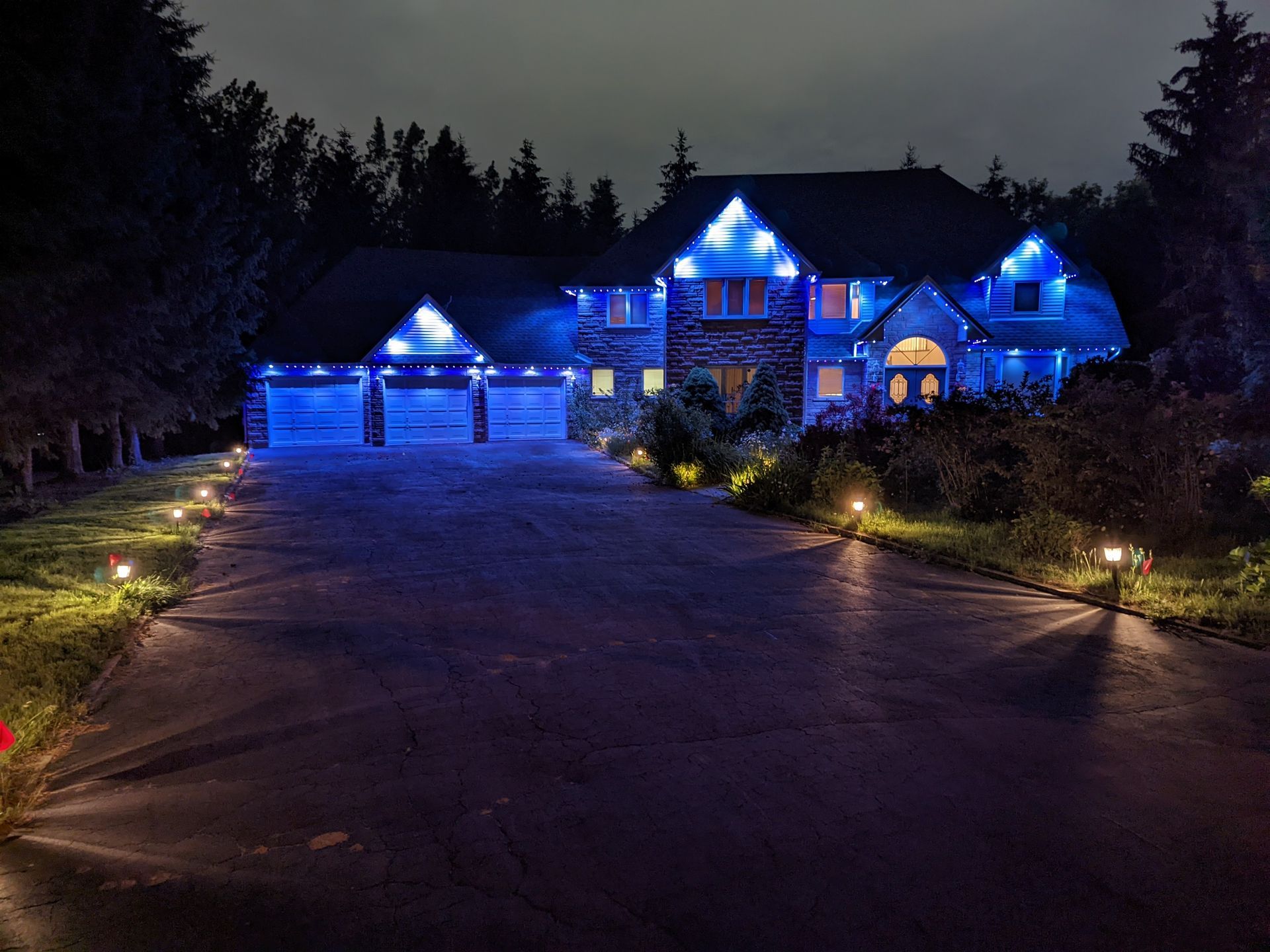 Large house and garage lit in blue at night, with a driveway leading through the front yard
