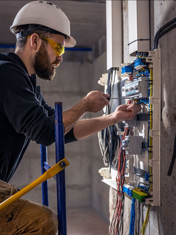 A man wearing a hard hat and goggles is working on an electrical box.
