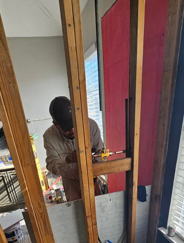 Worker using a power drill on wooden framing inside a partially finished room with pink and blue walls