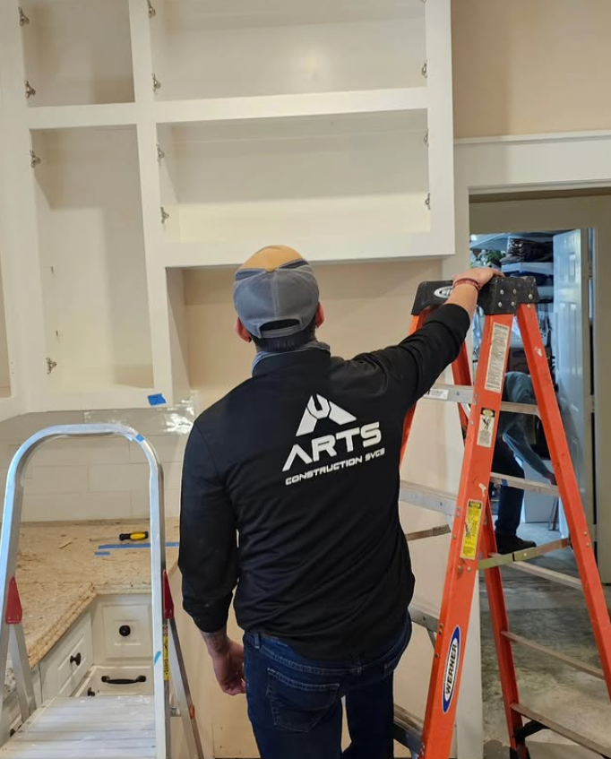 Worker in black shirt adjusting cabinets on an orange ladder in a kitchen under renovation