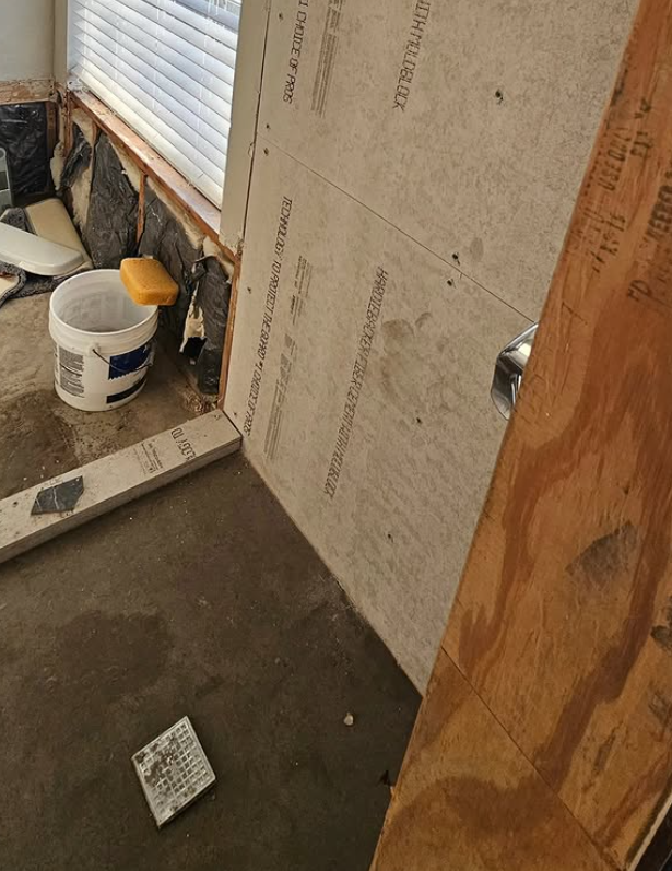Interior corner with unfinished wall, white bucket, and tools beside a rolled-down shutter