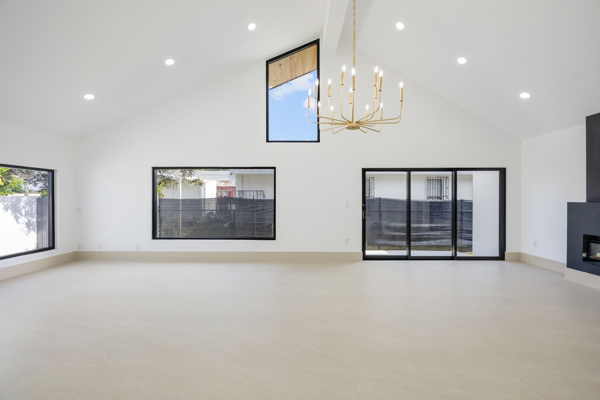 Bright open empty living room with white walls, chandelier, large windows, and sliding glass doors