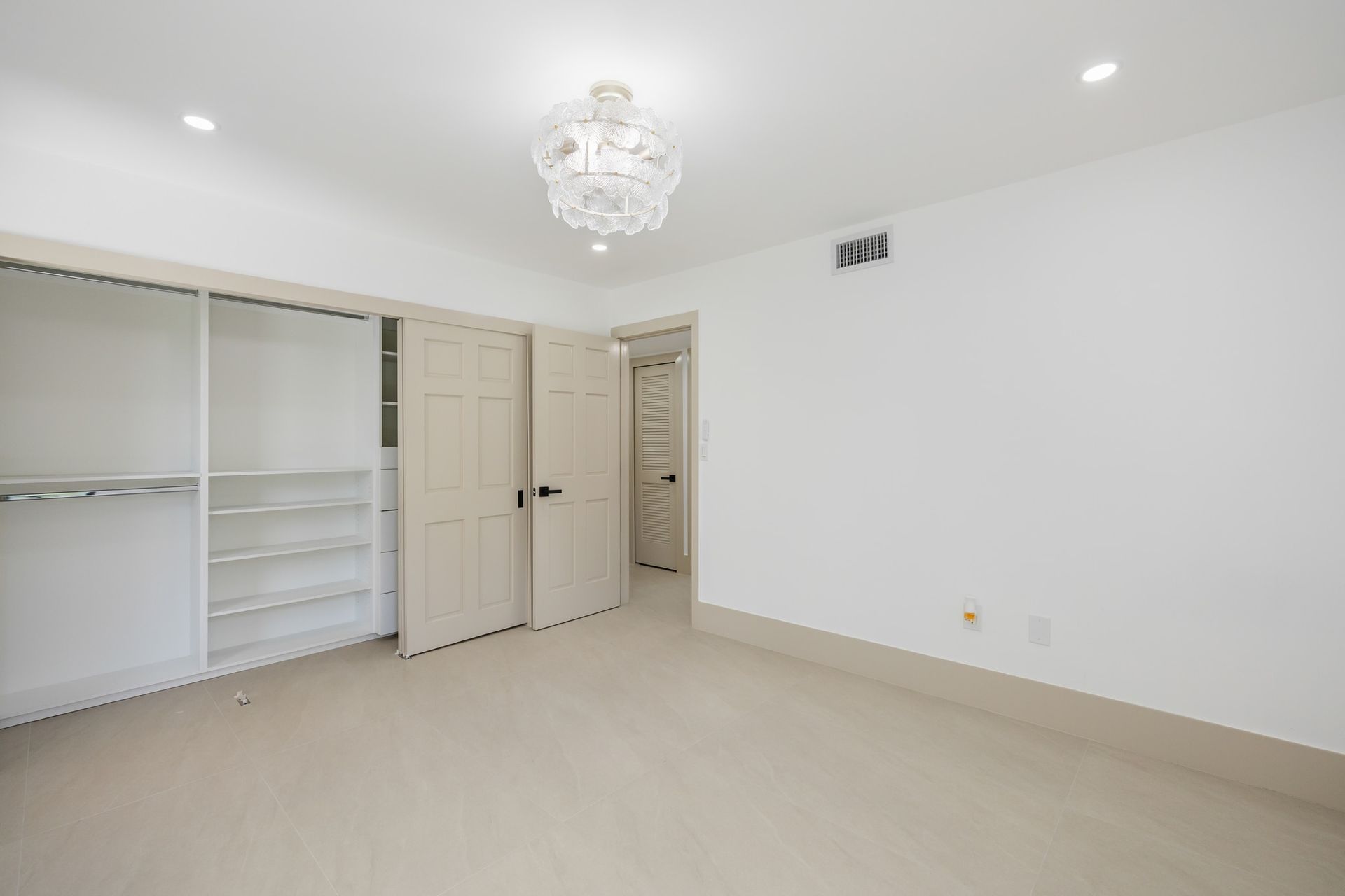 Empty white bedroom with chandelier, beige carpet, and open closet doors