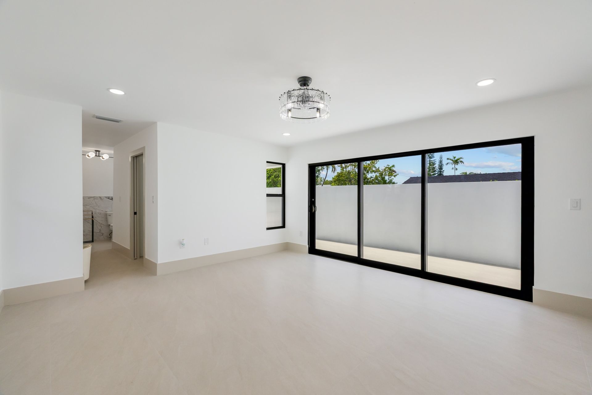 Empty white living room with beige carpet, recessed lights, and a doorway to a hallway.