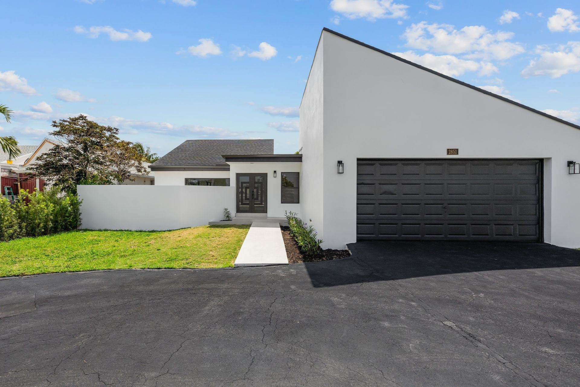 Modern white house with black garage door, driveway, and green lawn under a blue sky