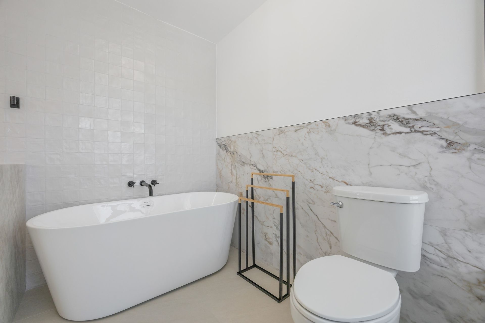 Modern bathroom with freestanding tub, toilet, marble wall, and gold towel rack