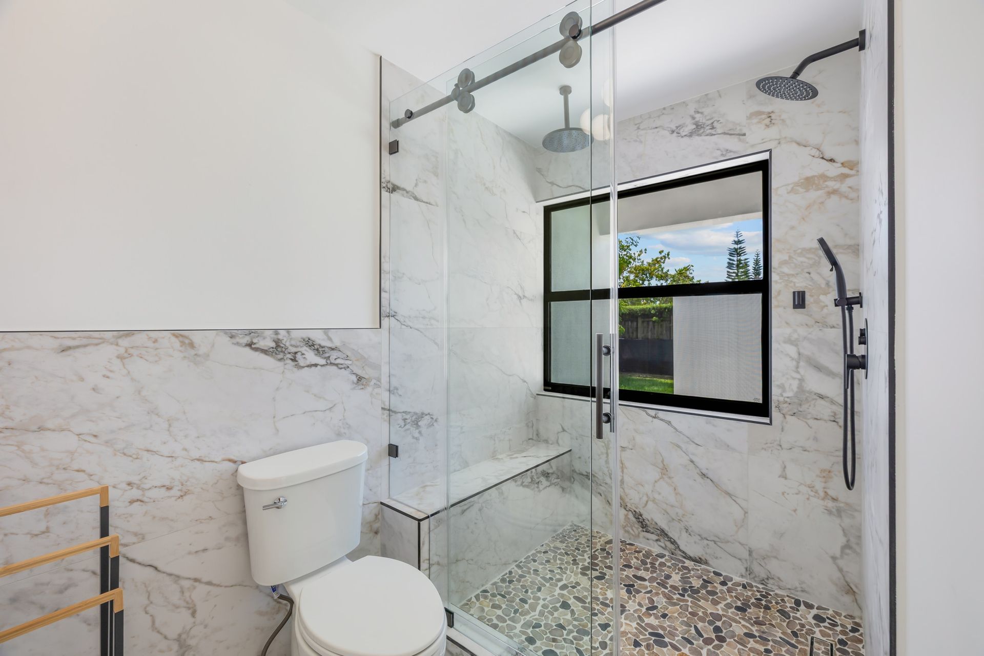 Modern marble-tiled bathroom with glass shower, white toilet, and pebble shower floor