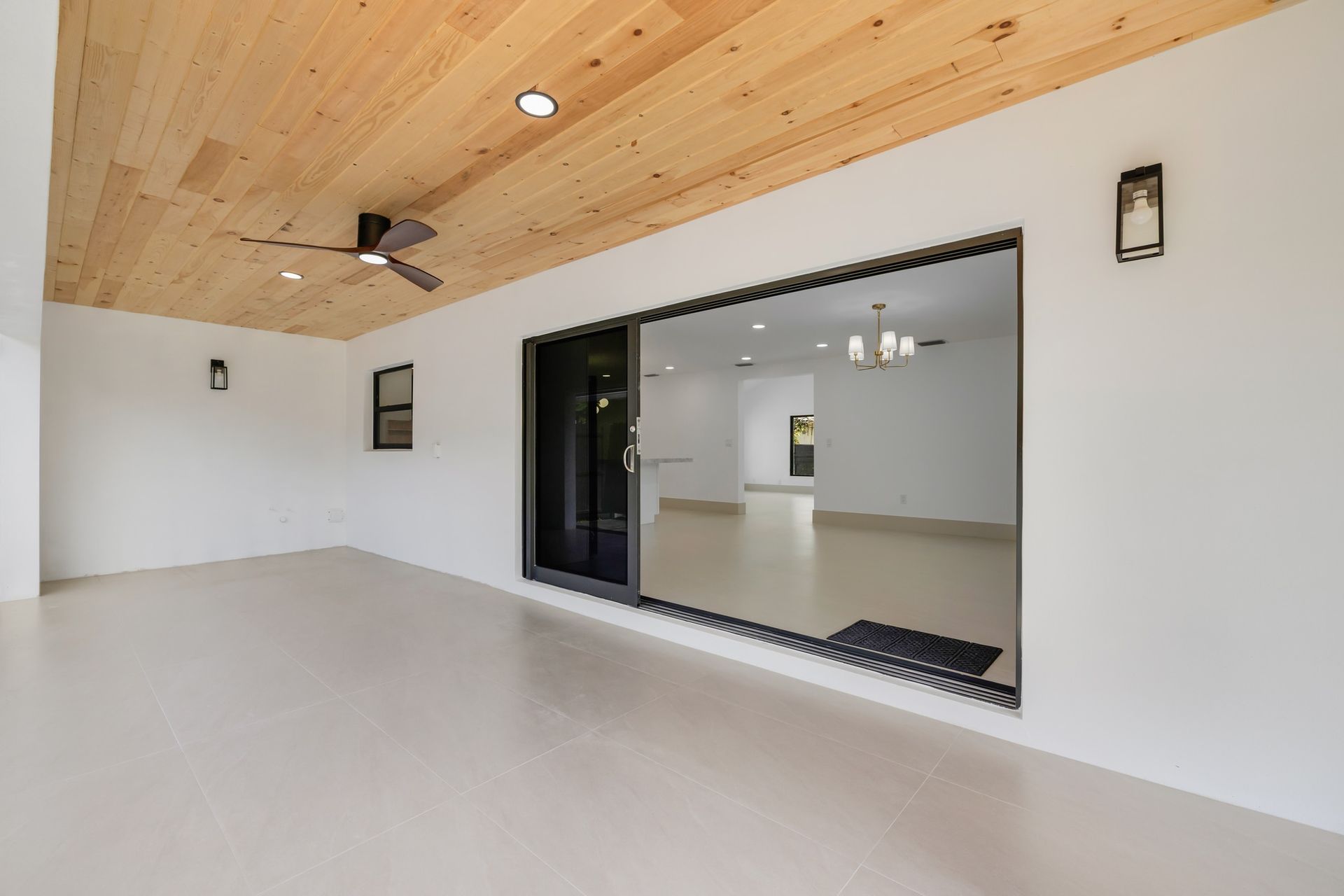 Modern covered patio with white walls, wood ceiling, sliding glass doors, and a concrete floor