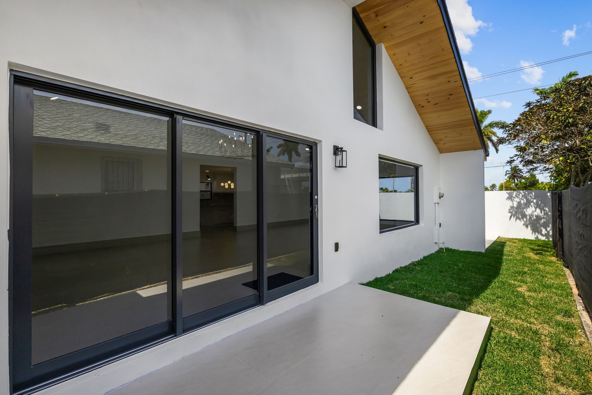 Modern white house exterior with sliding glass doors, a narrow side yard, and a wooden roof overhang