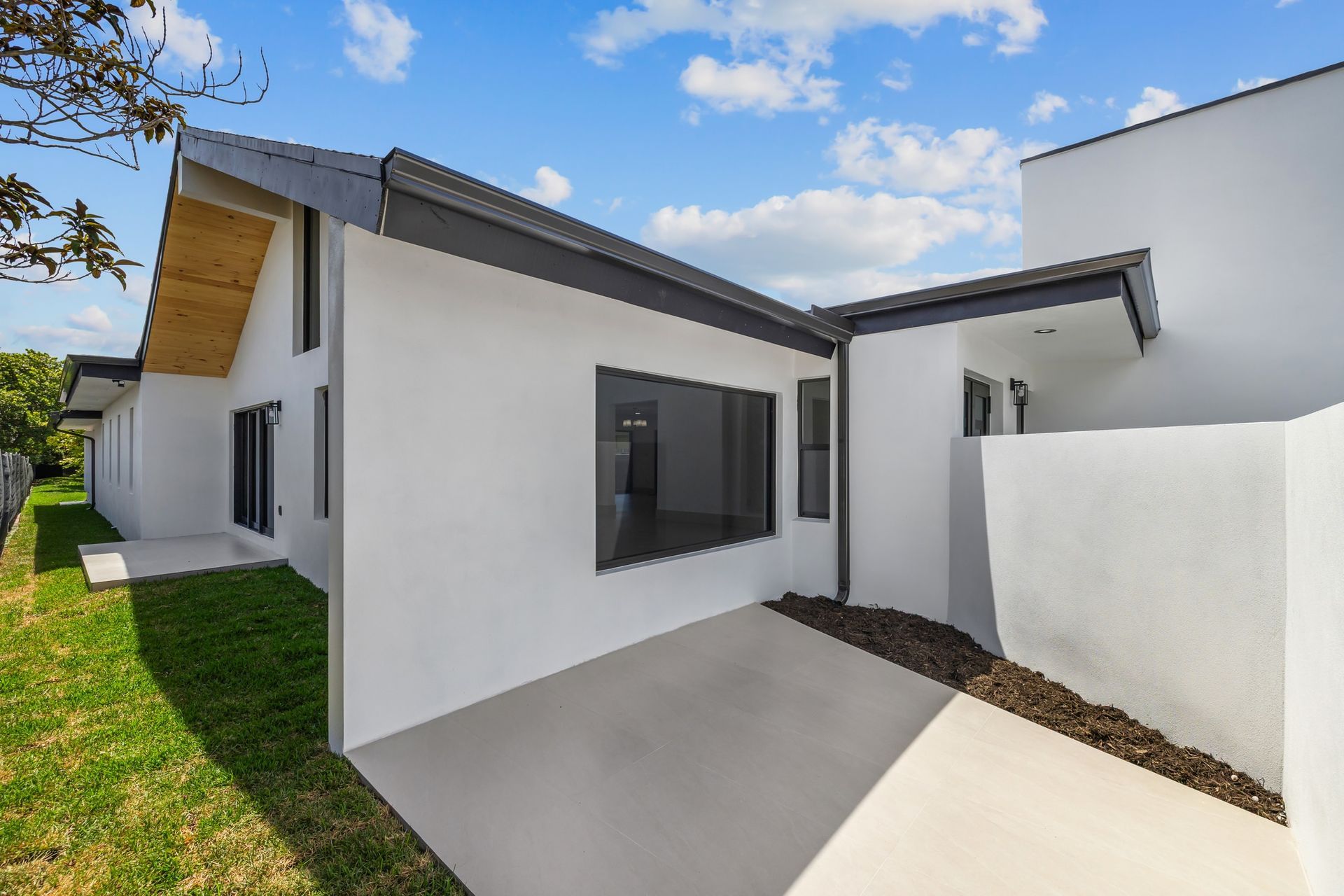 Modern white house exterior with gray windows, small patio, and grassy yard under a blue sky