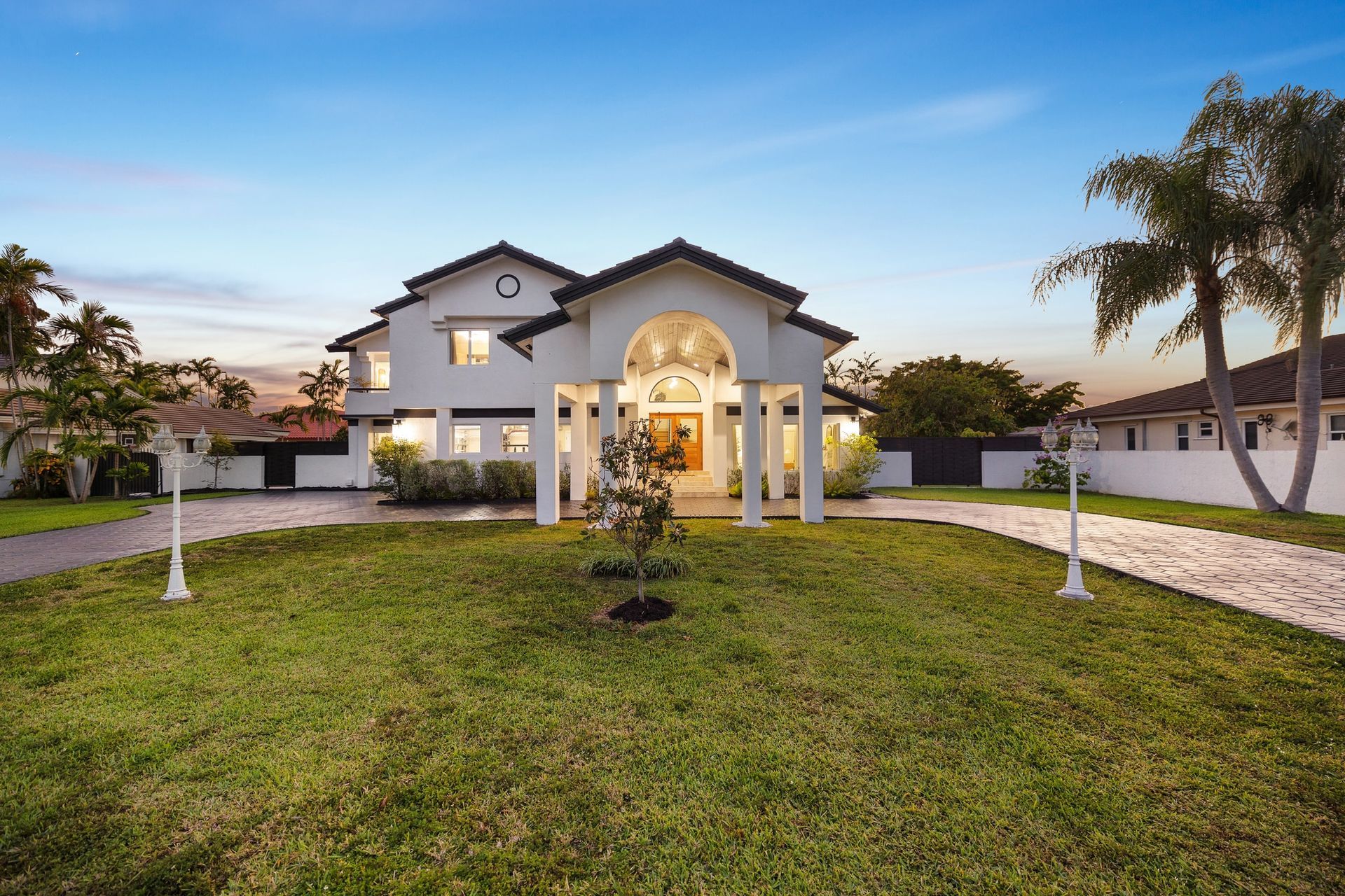 Solara, Large white suburban house with a manicured lawn, palm trees, and a curved driveway at sunset