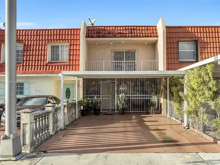 Two-story townhouse with red tile roof, barred windows, and a gated driveway under a covered carport.