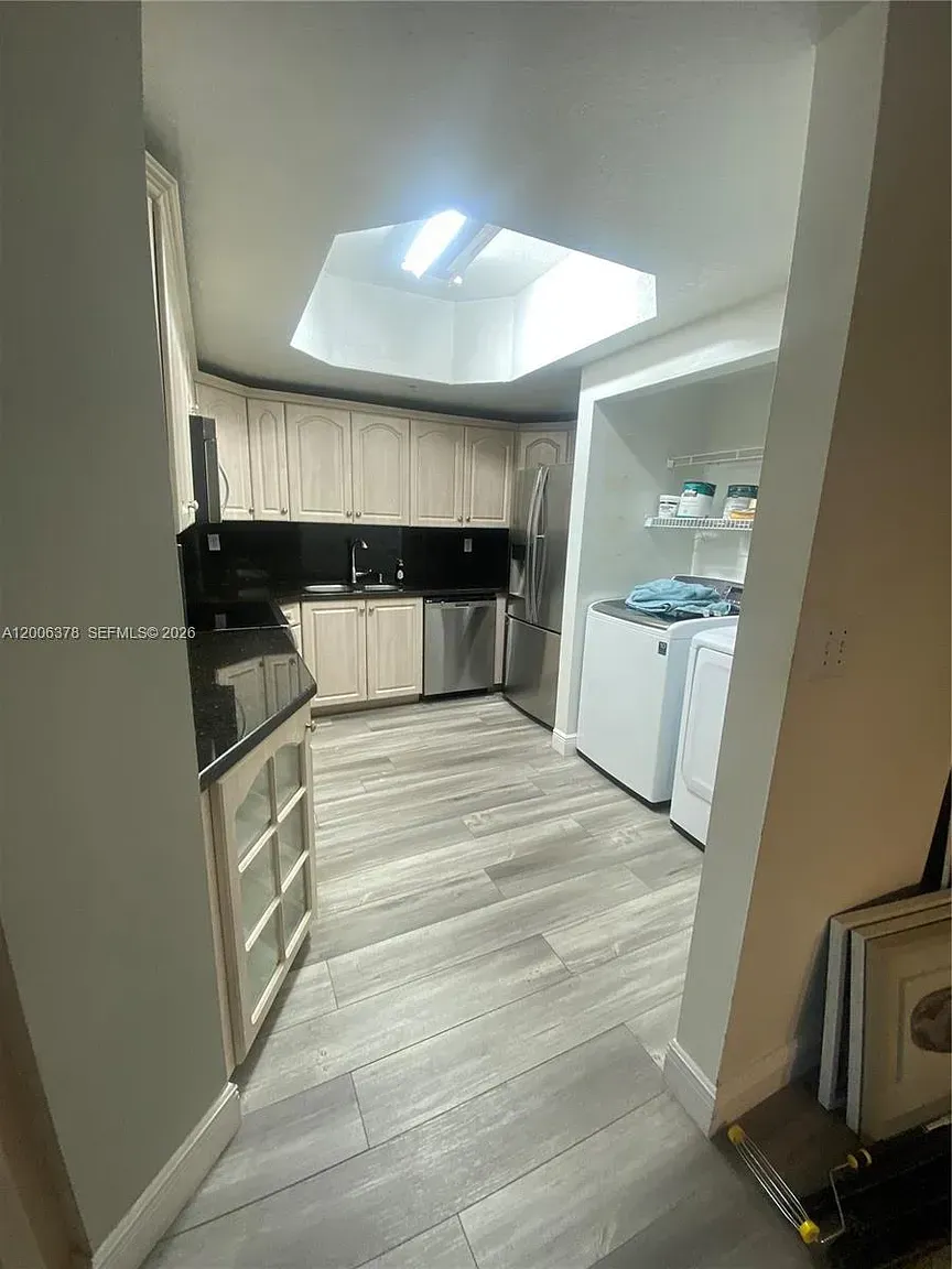 Small kitchen with skylight, wood cabinets, black countertops, and white appliances.