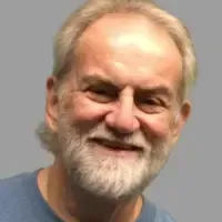 Smiling bearded man with short gray hair against a plain gray background