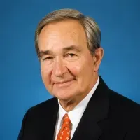 Portrait of a man in a black suit and orange tie against a blue background
