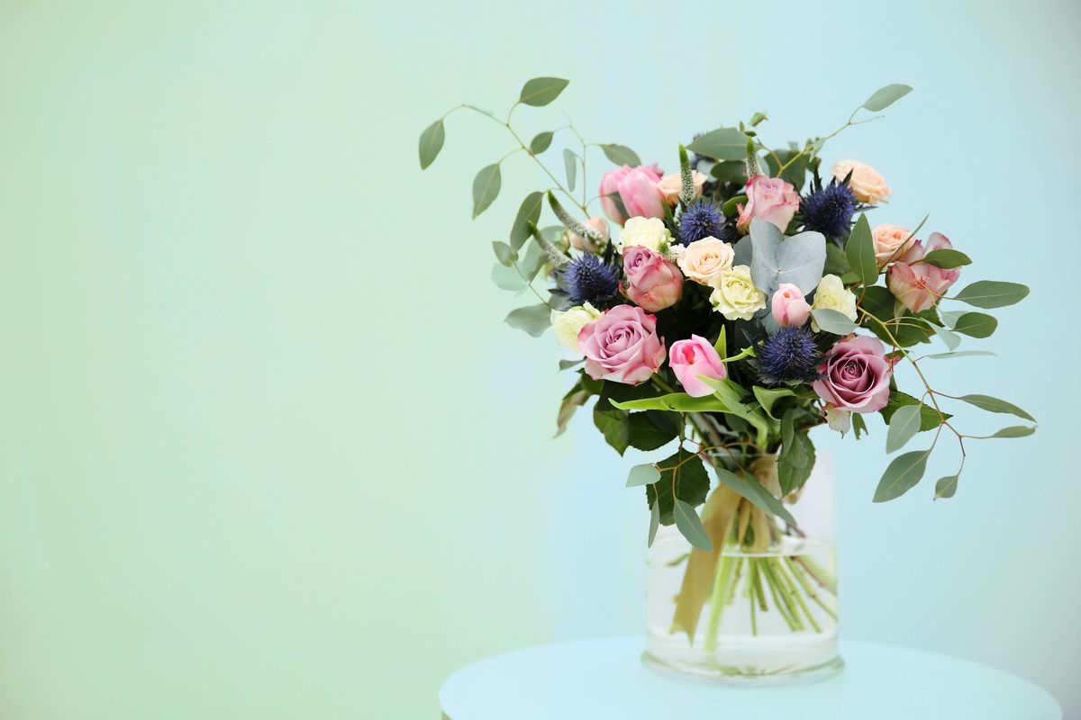 Bouquet of pink, cream, and white flowers in a glass vase on a white table against a pastel green background