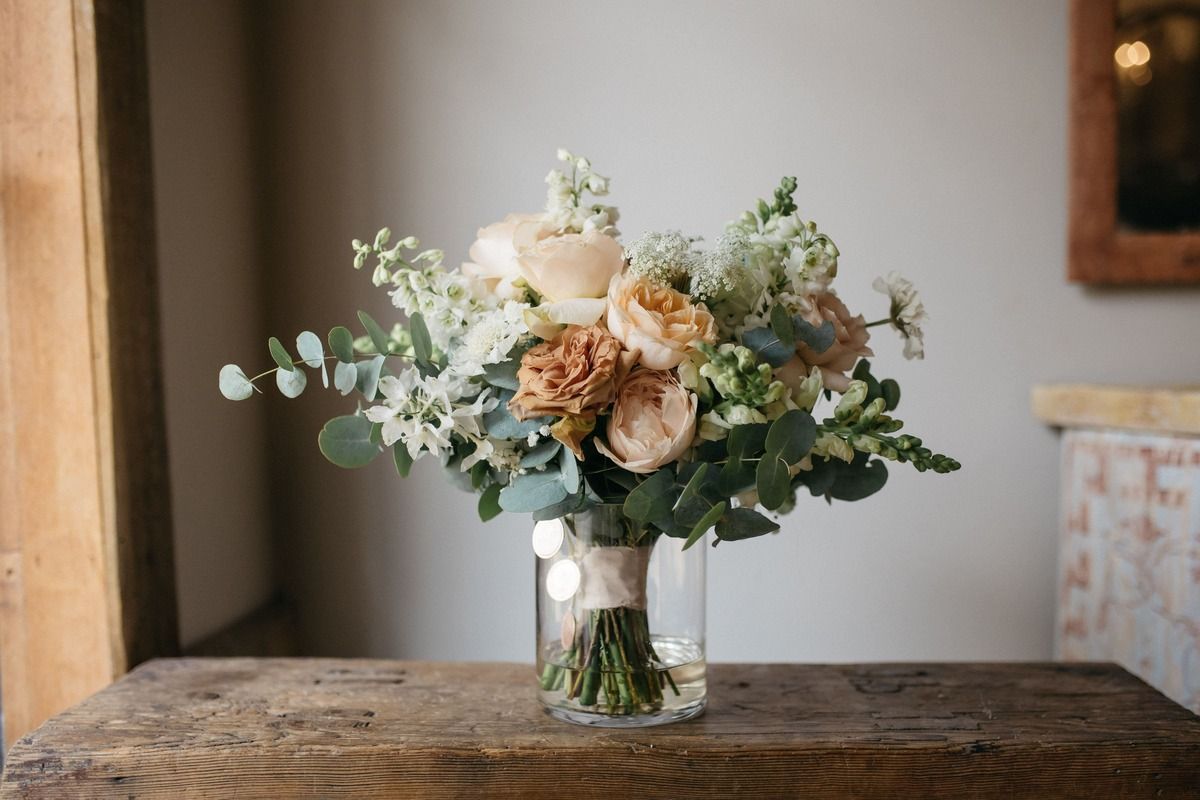 Bouquet of pale flowers and greenery in a glass vase on a rustic wooden table by a window