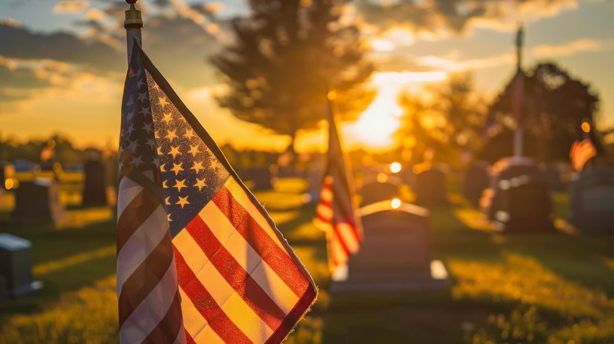 American flags at sunset in a cemetery, with warm golden light and blurred graves in the background.