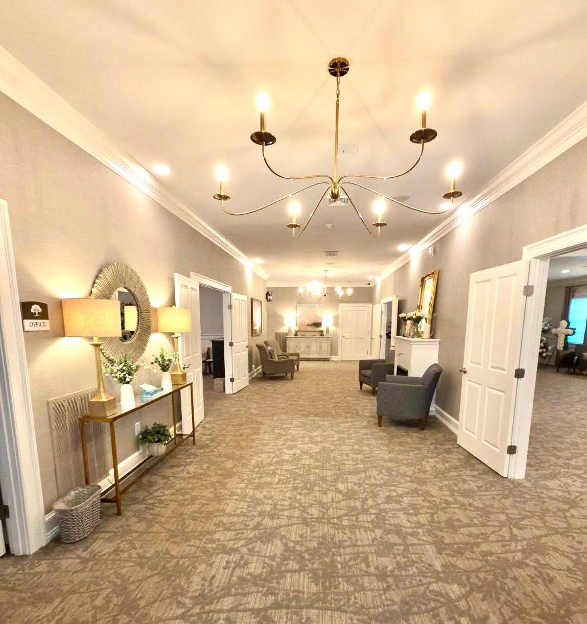 Elegant hotel lobby hallway with chandelier, patterned carpet, wall lamps, and seating area