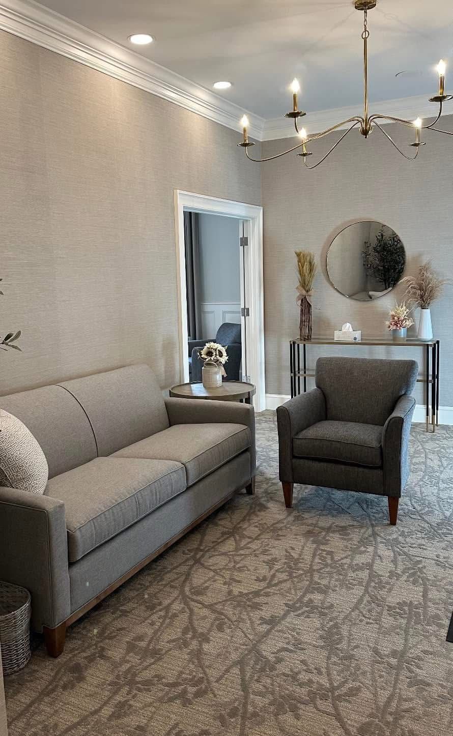 Elegant living room with gray sofa, armchair, chandelier, mirror, and patterned rug