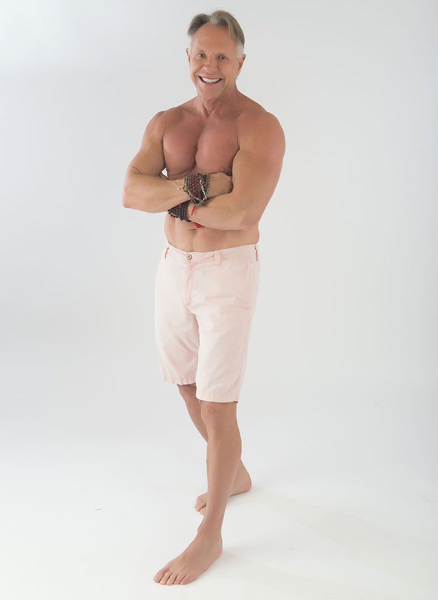 A shirtless man in pink shorts is standing with his arms crossed.