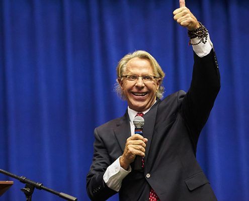 A man in a suit is giving a thumbs up while holding a microphone