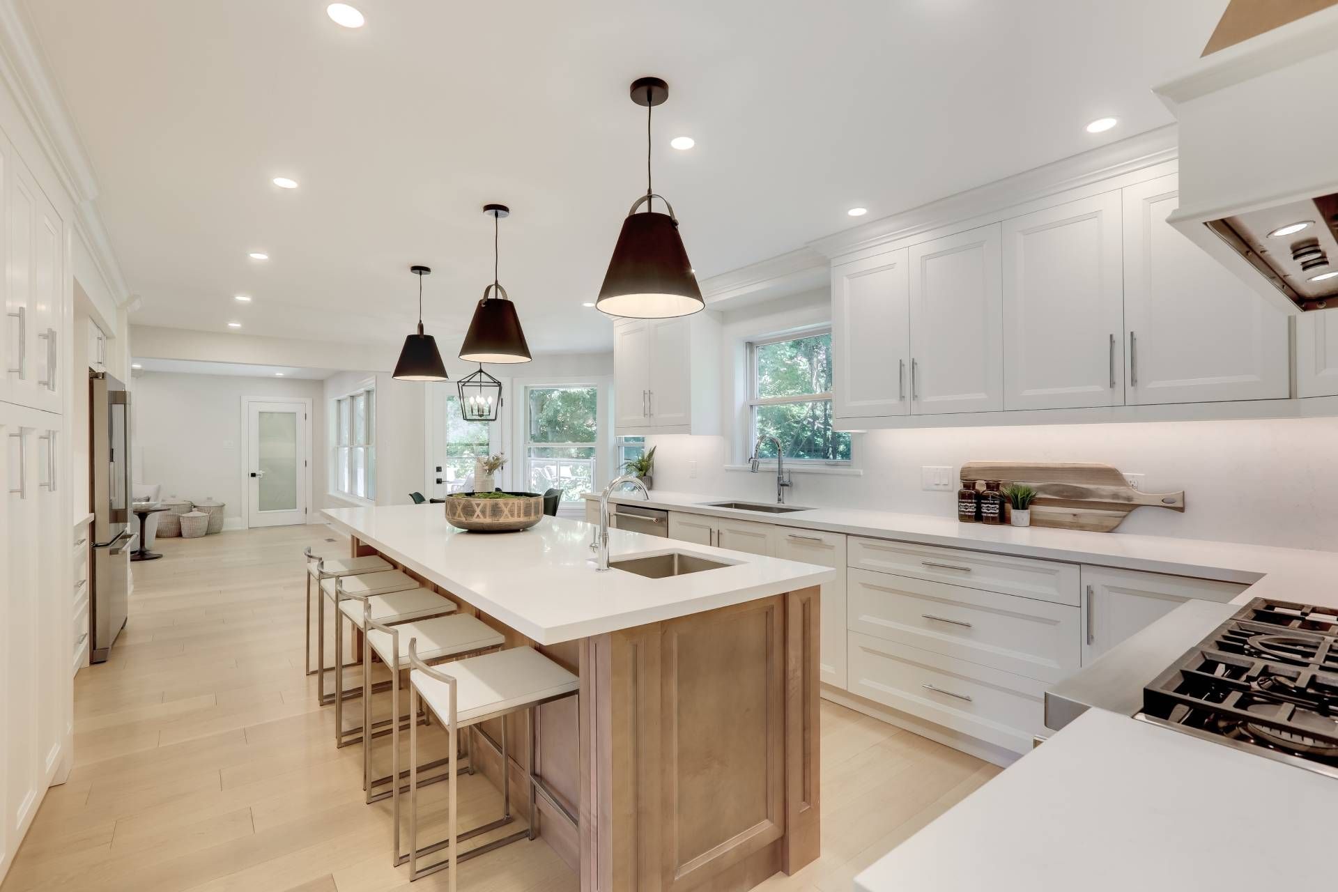 Bright modern white kitchen with island, barstools, pendant lights, and stainless steel appliances