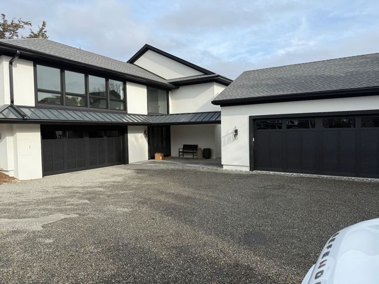 Modern two-story house with black garage doors, gravel driveway, and cloudy sky