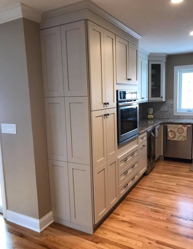 Modern kitchen with tall beige cabinets, built-in oven, hardwood floor, and a window over the sink.