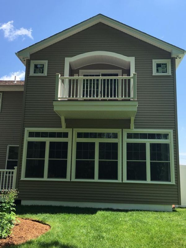 Two-story gray house with green trim, a small balcony, and a grassy front yard under a blue sky