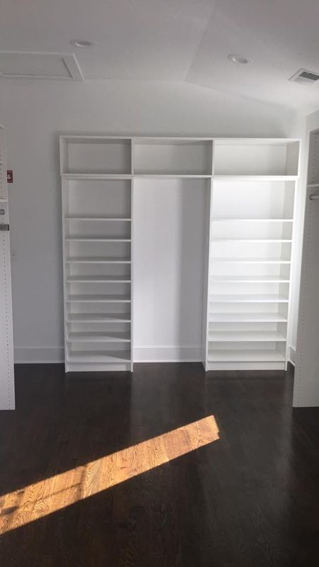 Empty room with white built-in shelves and a dark wood floor, lit by sunlight.
