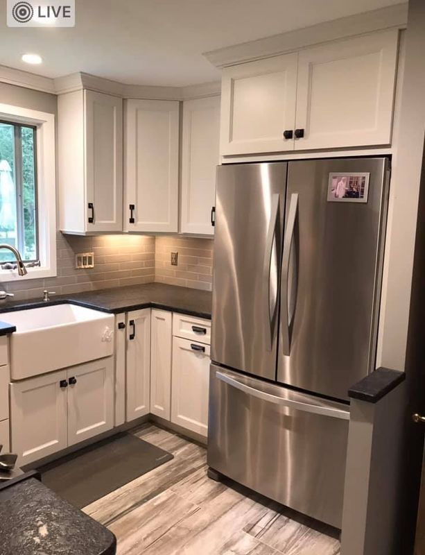 Modern white kitchen with stainless steel refrigerator, black countertops, and wood-look floor tiles.