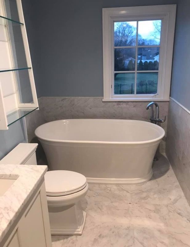 Modern bathroom with freestanding tub, toilet, marble floor, and window at dusk