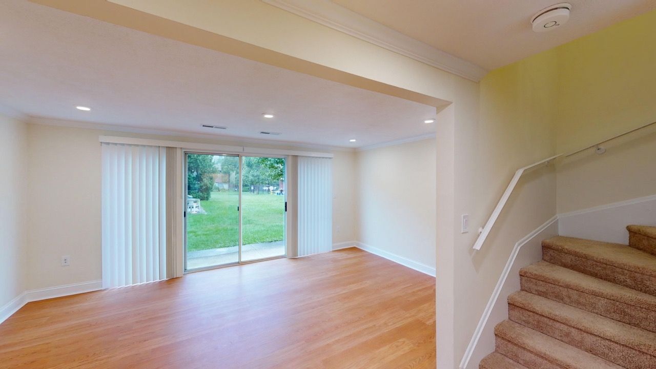 Bright living area with sliding glass doors to the backyard, light wood floors, and a carpeted staircase.