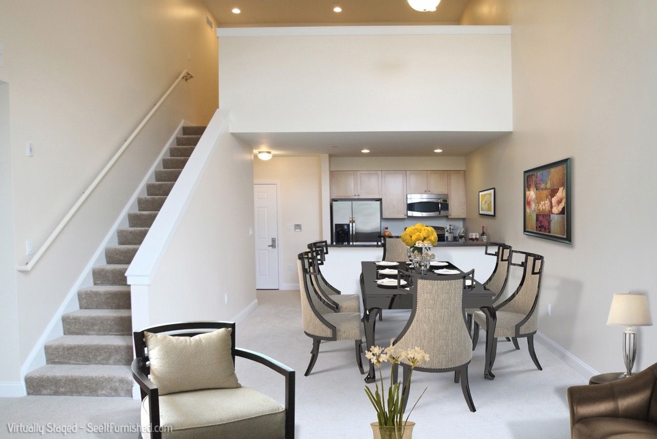 Open-concept dining area with a long dark table, beige chairs, staircase on the left, and a modern kitchen behind.