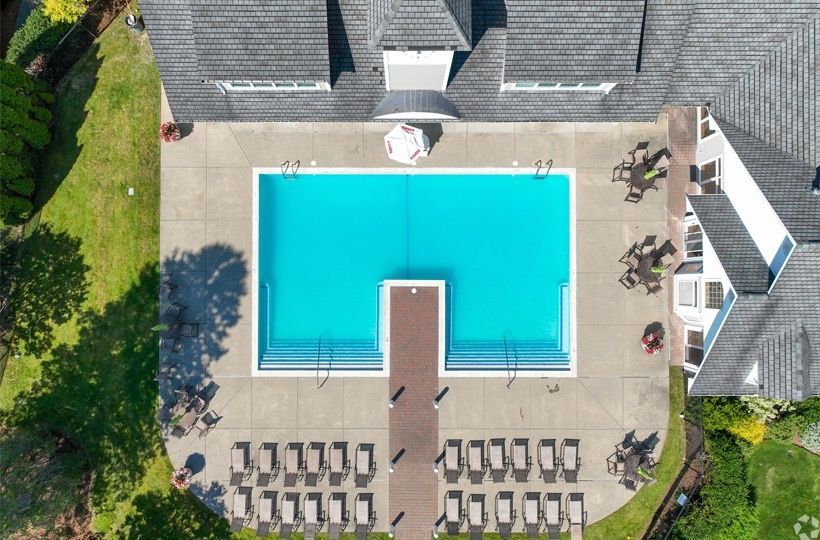 Aerial view of a rectangular pool at a multifamily property, surrounded by lounge chairs and buildings.