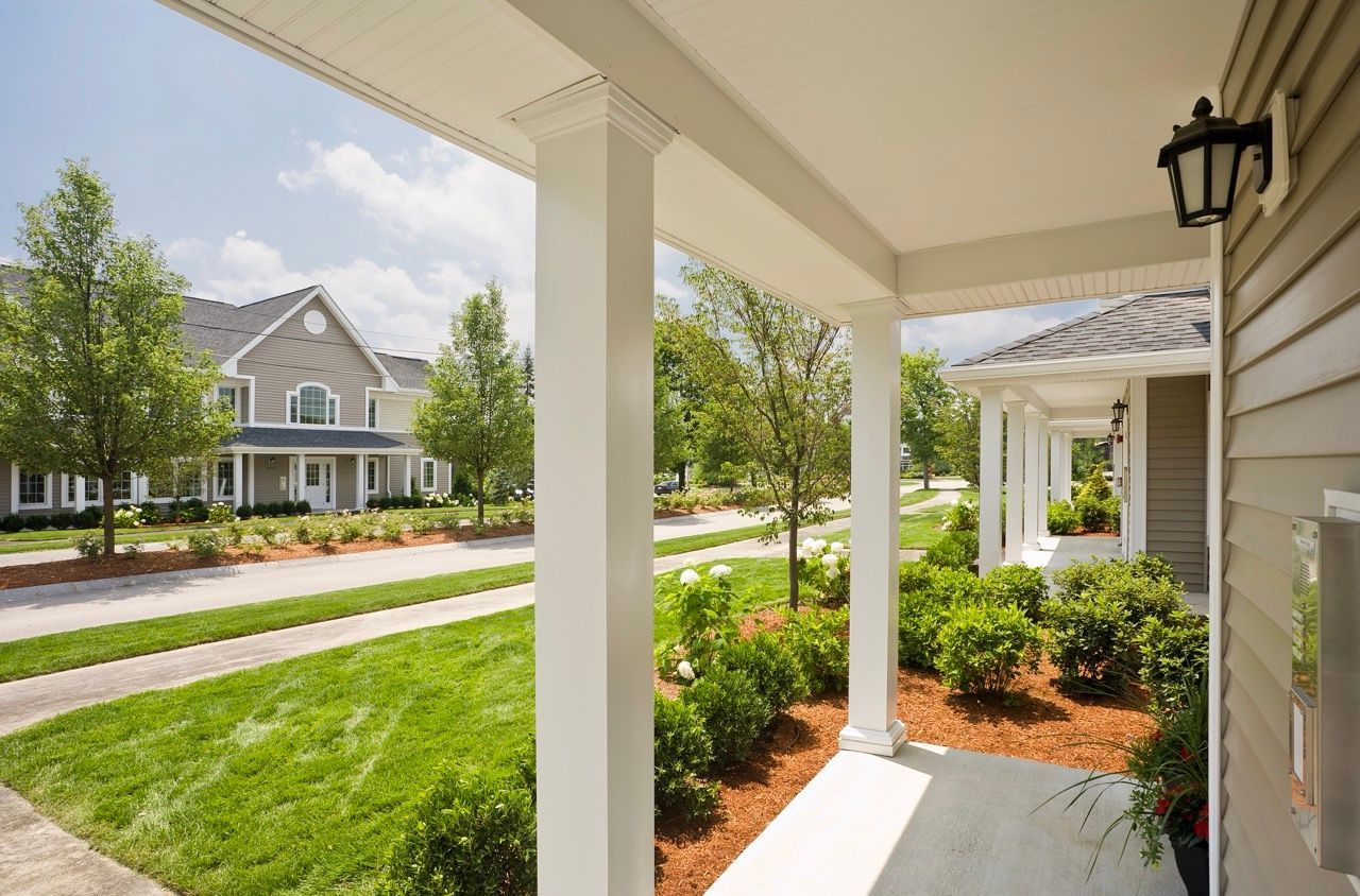 Covered walkway with white columns and landscaped front yards at an apartment community.