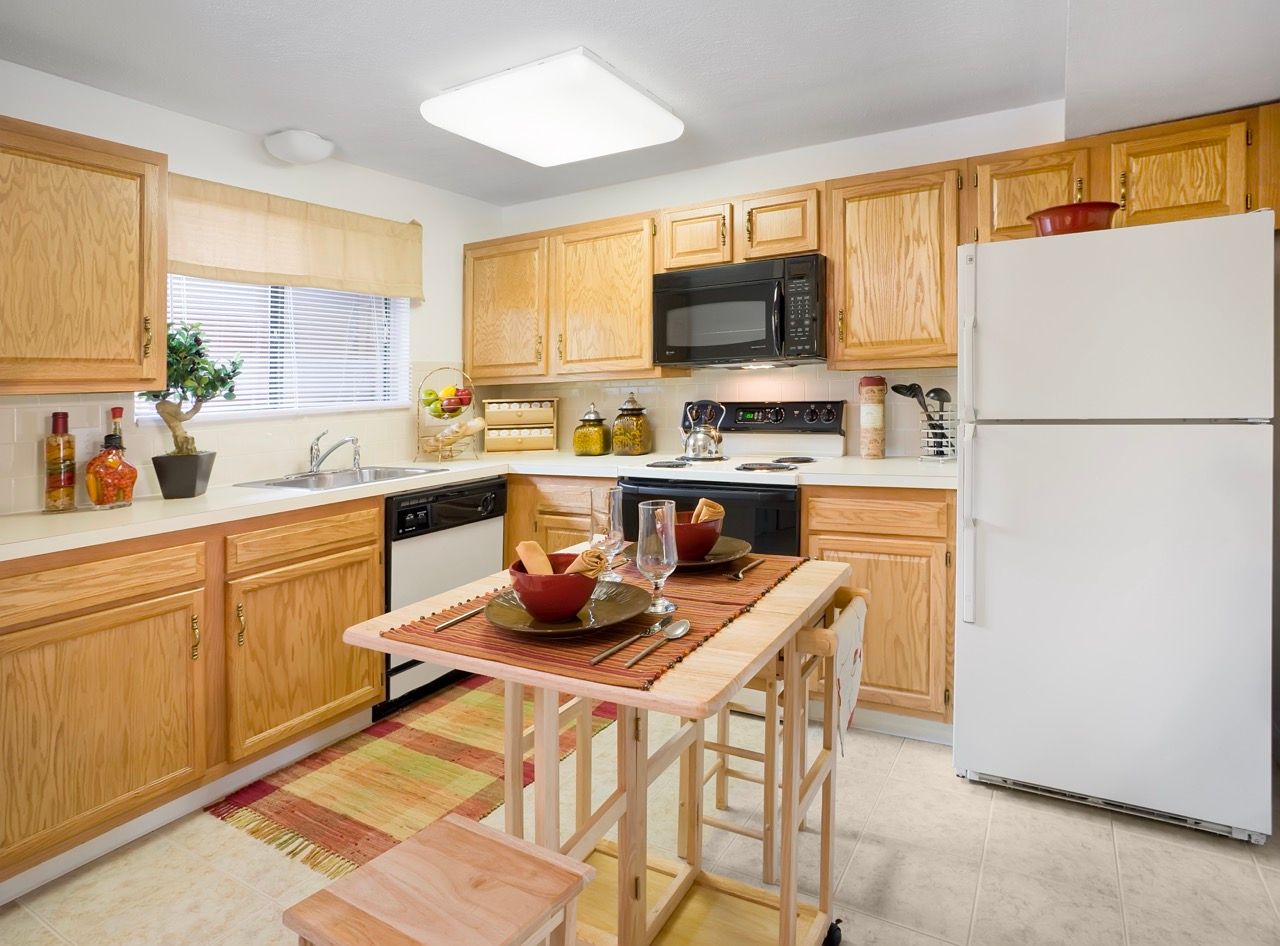 Bright kitchen in an apartment with wooden cabinets, white appliances, and a small central island.