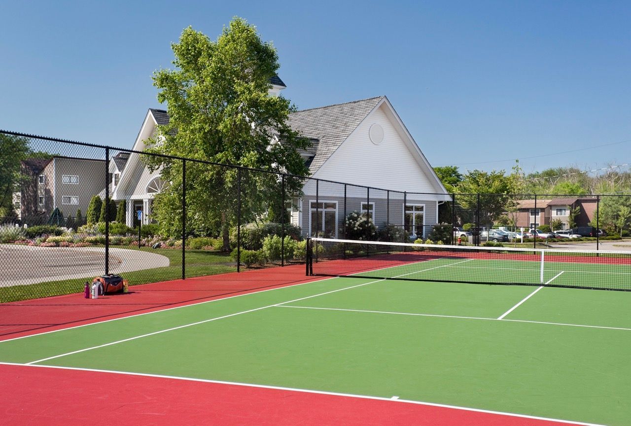 Outdoor community tennis court with a fence and clubhouse in the background.