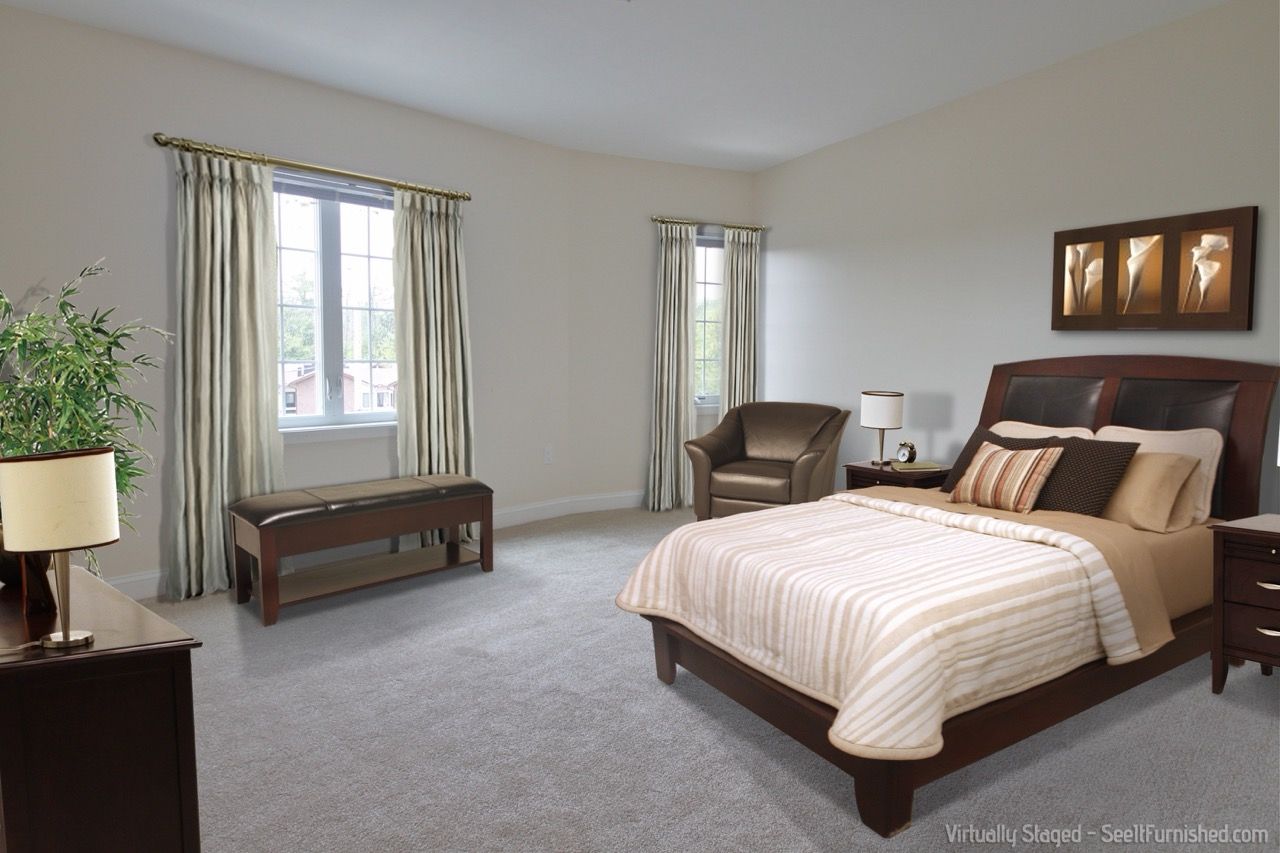 Bedroom in a staged apartment with a large bed, bench by window, and seating area.