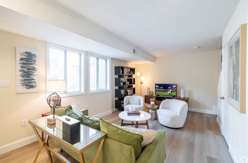Living room in a modern apartment with a green sofa, white chairs, and a TV on a wooden stand.
