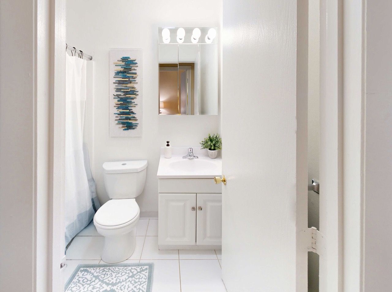 White apartment bathroom with toilet, vanity, mirror, and shower curtain.