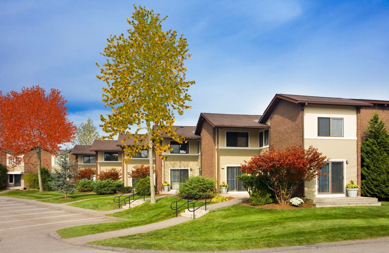 Exterior view of a multi-building apartment community with green lawn, sidewalks, and fall trees.
